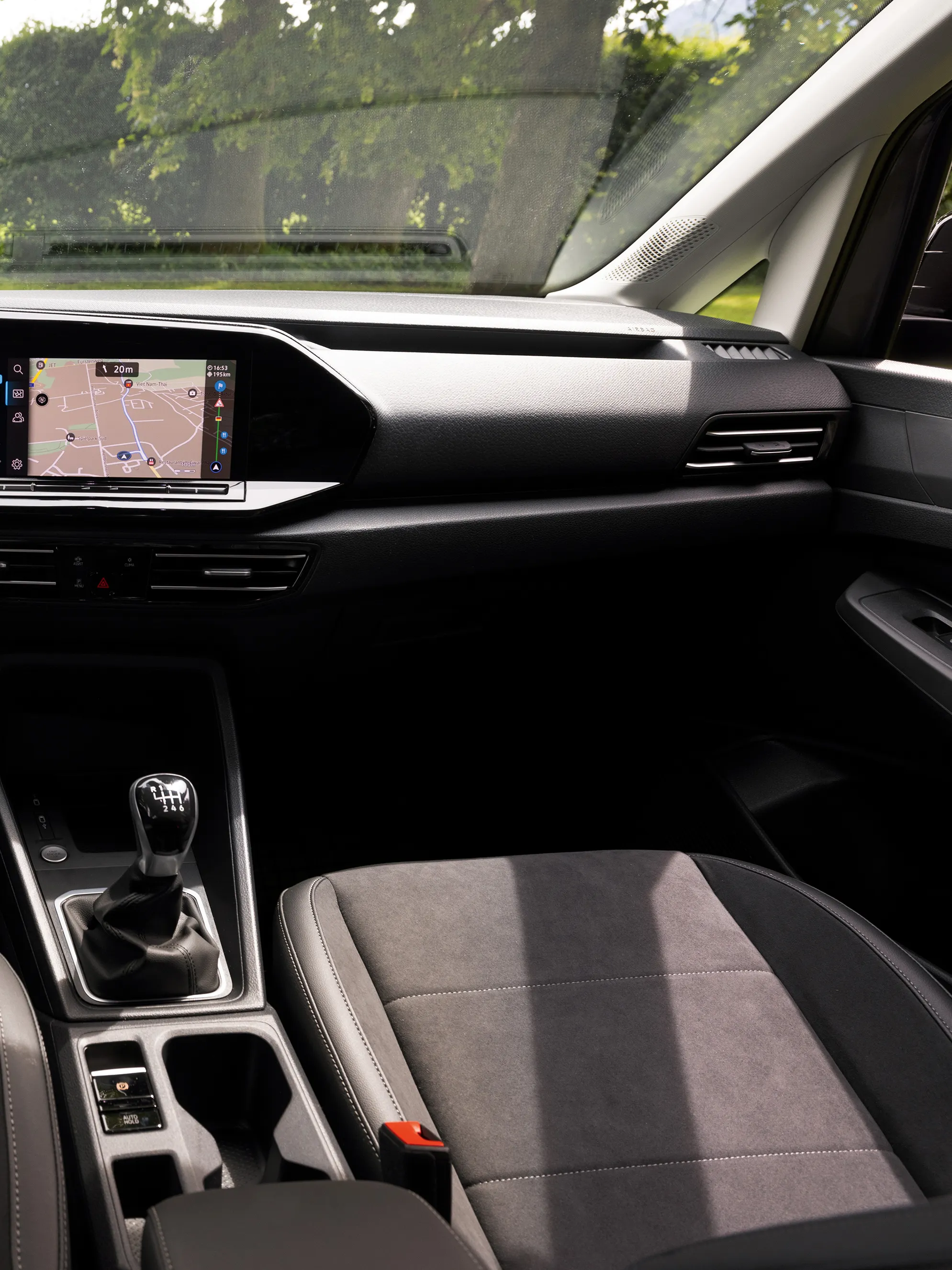 Interiér automobilu Volkswagen s logom na volante. Na palubnej doske sú dva veľké digitálne displeje, jeden prístrojového panela zobrazujúci informácie o vozidle a druhý systému infotainment s navigačným systémom. Sedadlá sú čalúnené tmavým materiálom.  Cez čelné  sklo je výhľad na rozsiahlu lúku, ktorú lemujú stromy.