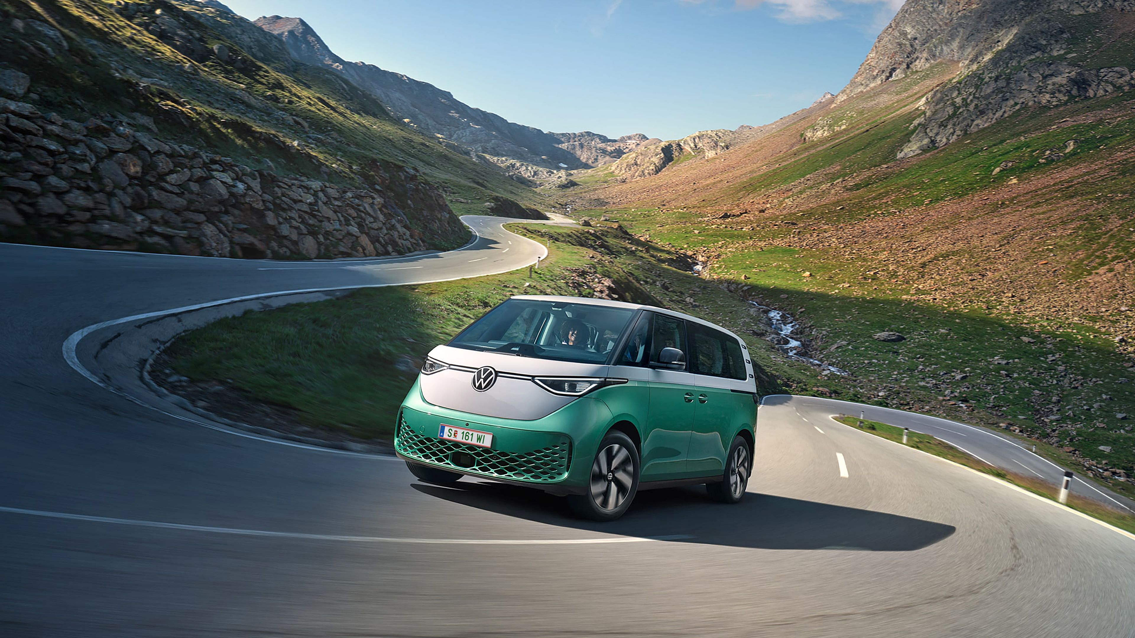 Ein grün weißer VW ID. Buzz fährt dynamisch in die Kurve einer kurvenreichen Bergstraße
