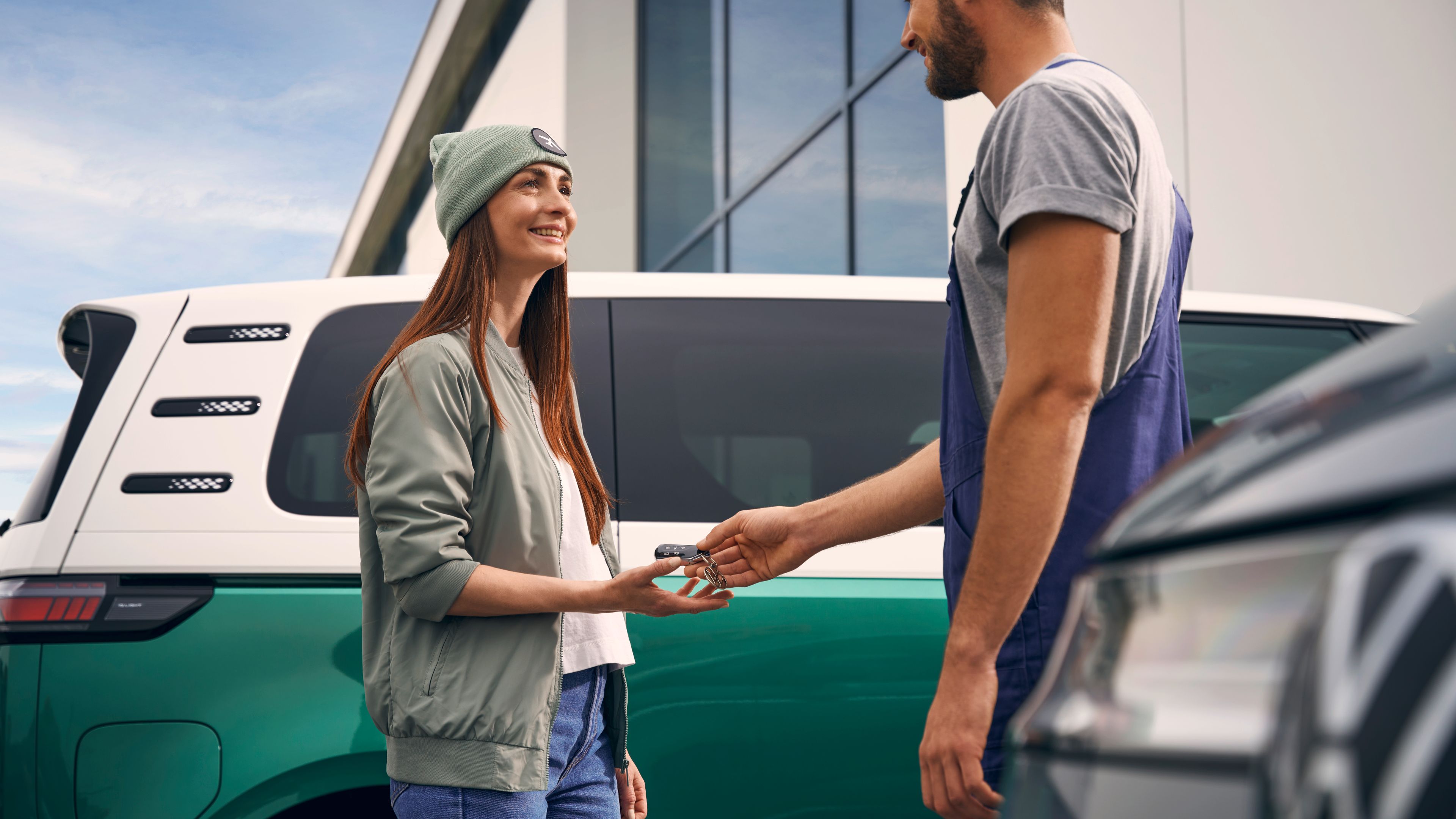 Servisný pracovník podáva mladej žene kľúč od vozidla, ktoré je zaparkované pred autorizovaným servisom Volkswagen.