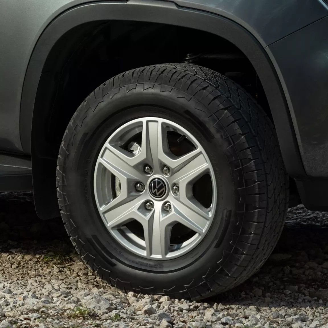 VW Amarok stojí na štrkovej ceste v lese. Detail na koleso, čiastočne vidieť predný nárazník a blatník.