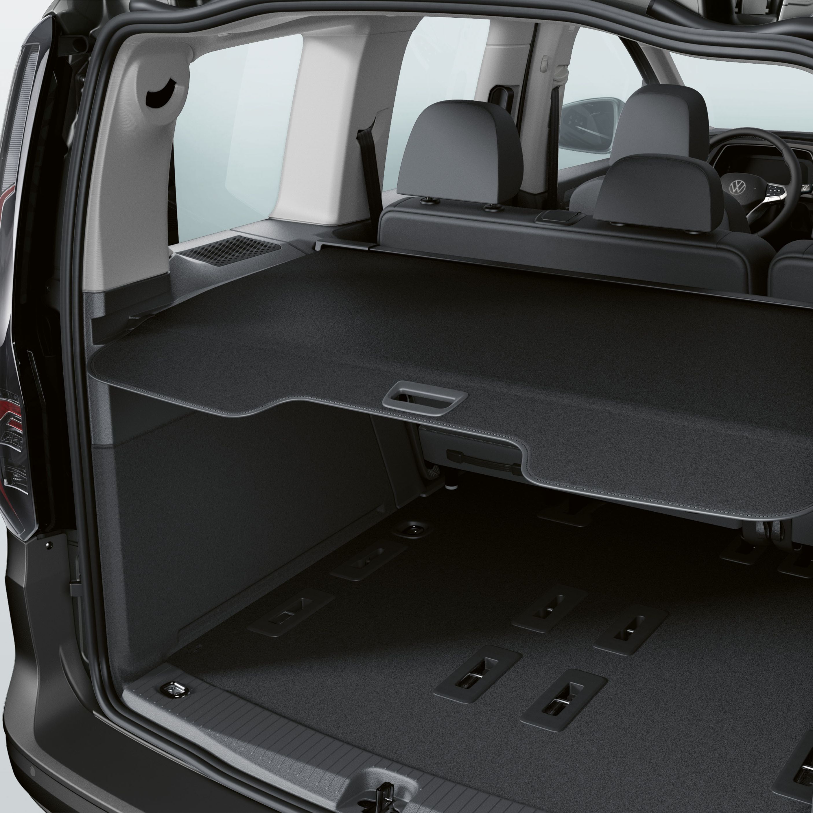 Pohľad do batožinového priestoru VW Caddy, kde je vidieť zadné sedadlá, veľký batožinový priestor a jeho kryt. Vnútro auta je moderné a priestranné.