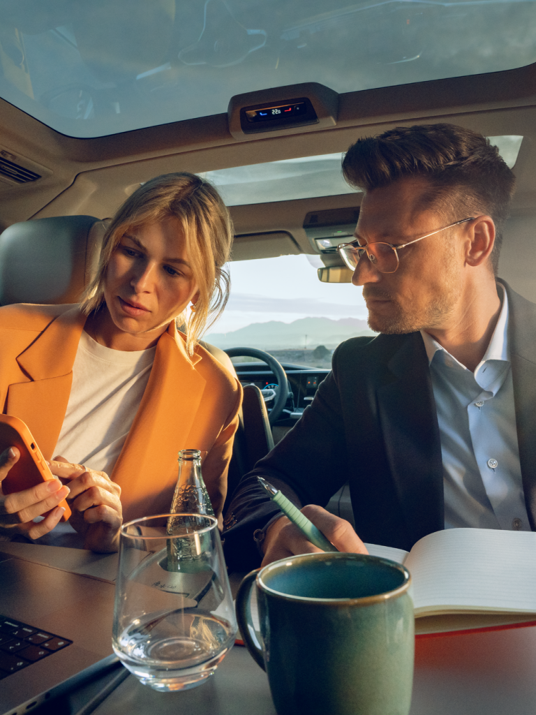 Mann und Frau sitzen im Fond eines neuen VW Multivans, ausgeklappter Tisch, schauen auf Laptop