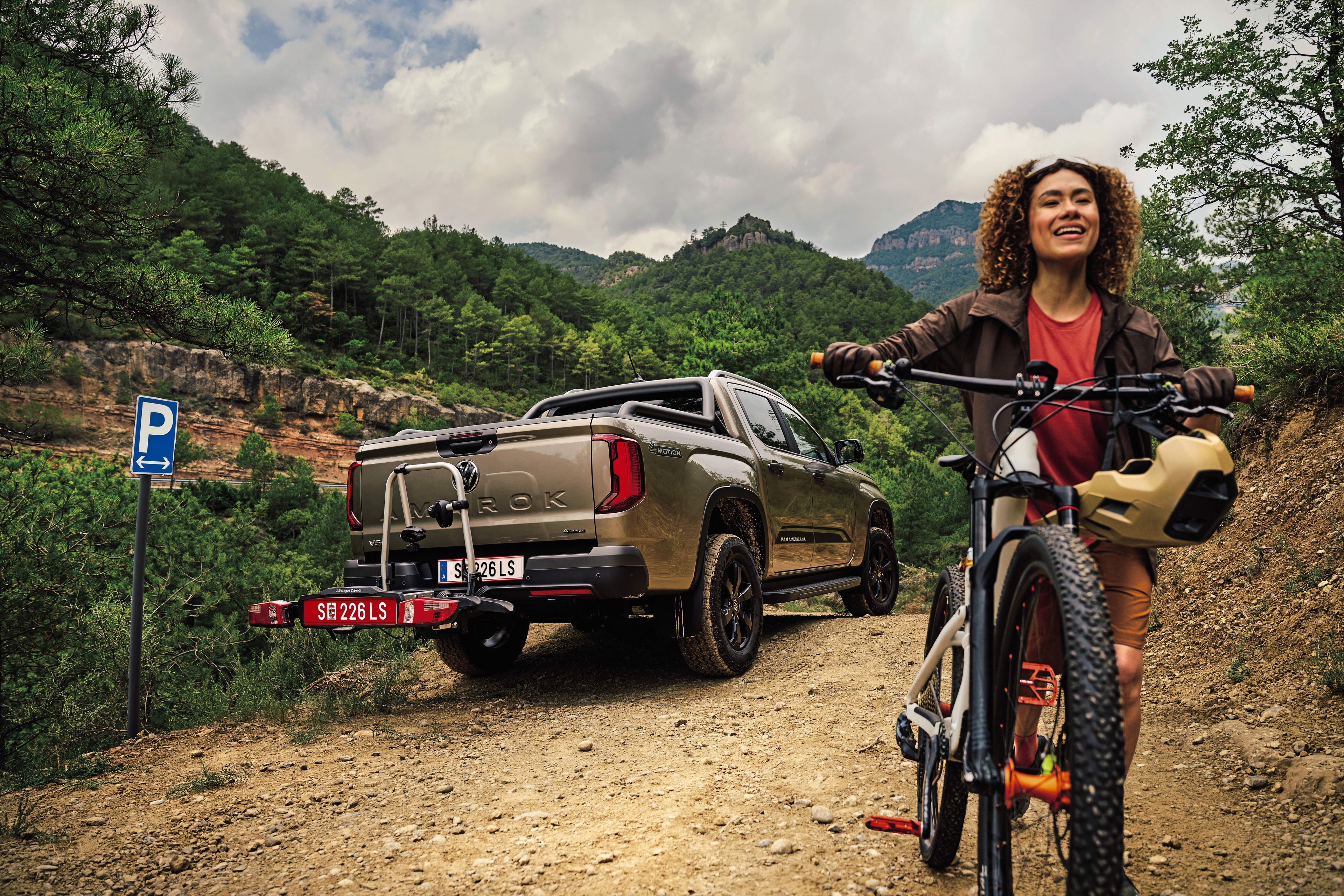 Amarok s nosičom bicyklov na ťažnom zariadení je zaparkovaný v lese, žena s horským bicyklom odchádza od neho preč. 