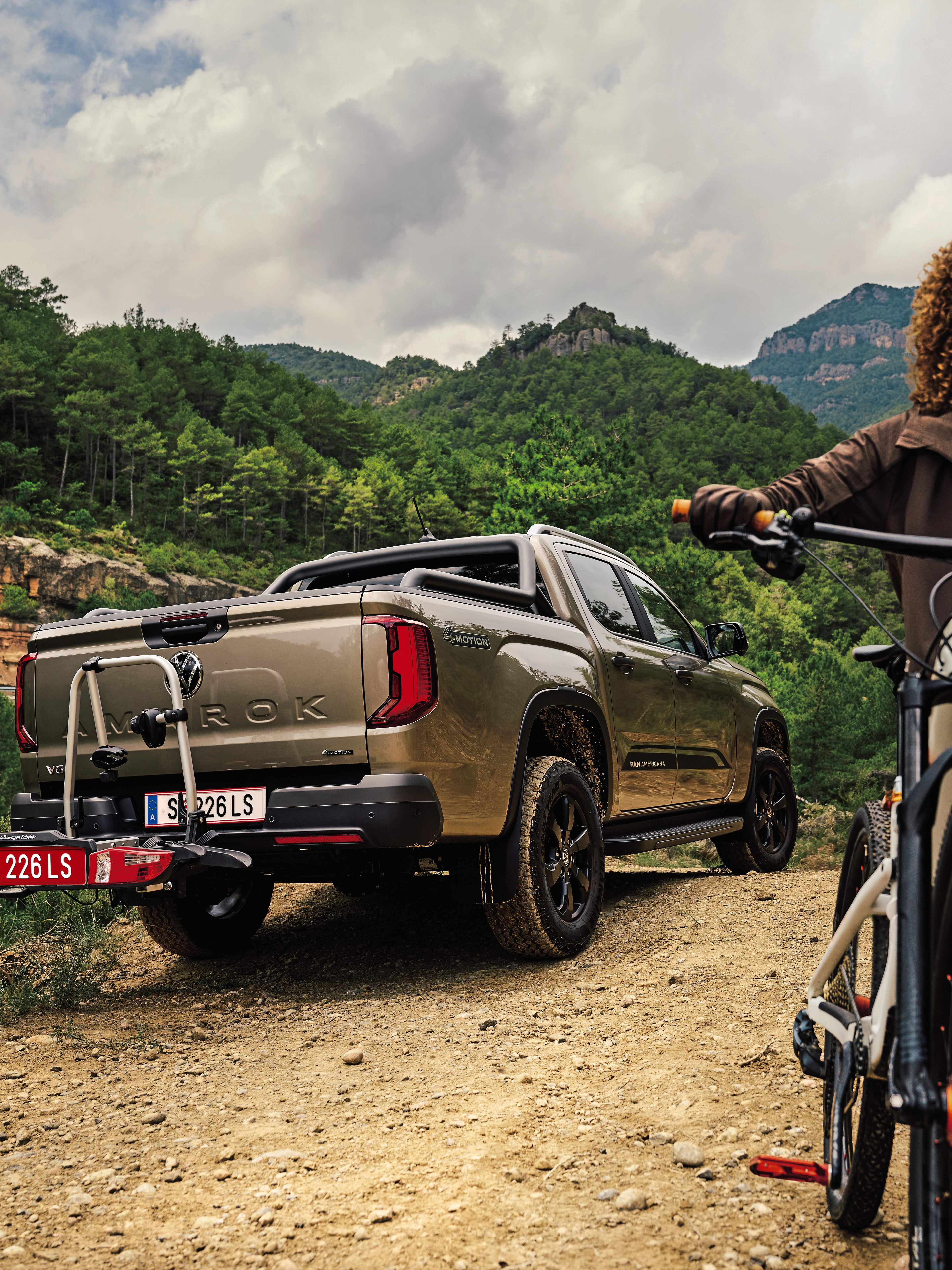 Amarok s nosičom bicyklov na ťažnom zariadení je zaparkovaný v lese, žena s horským bicyklom odchádza od neho preč. 