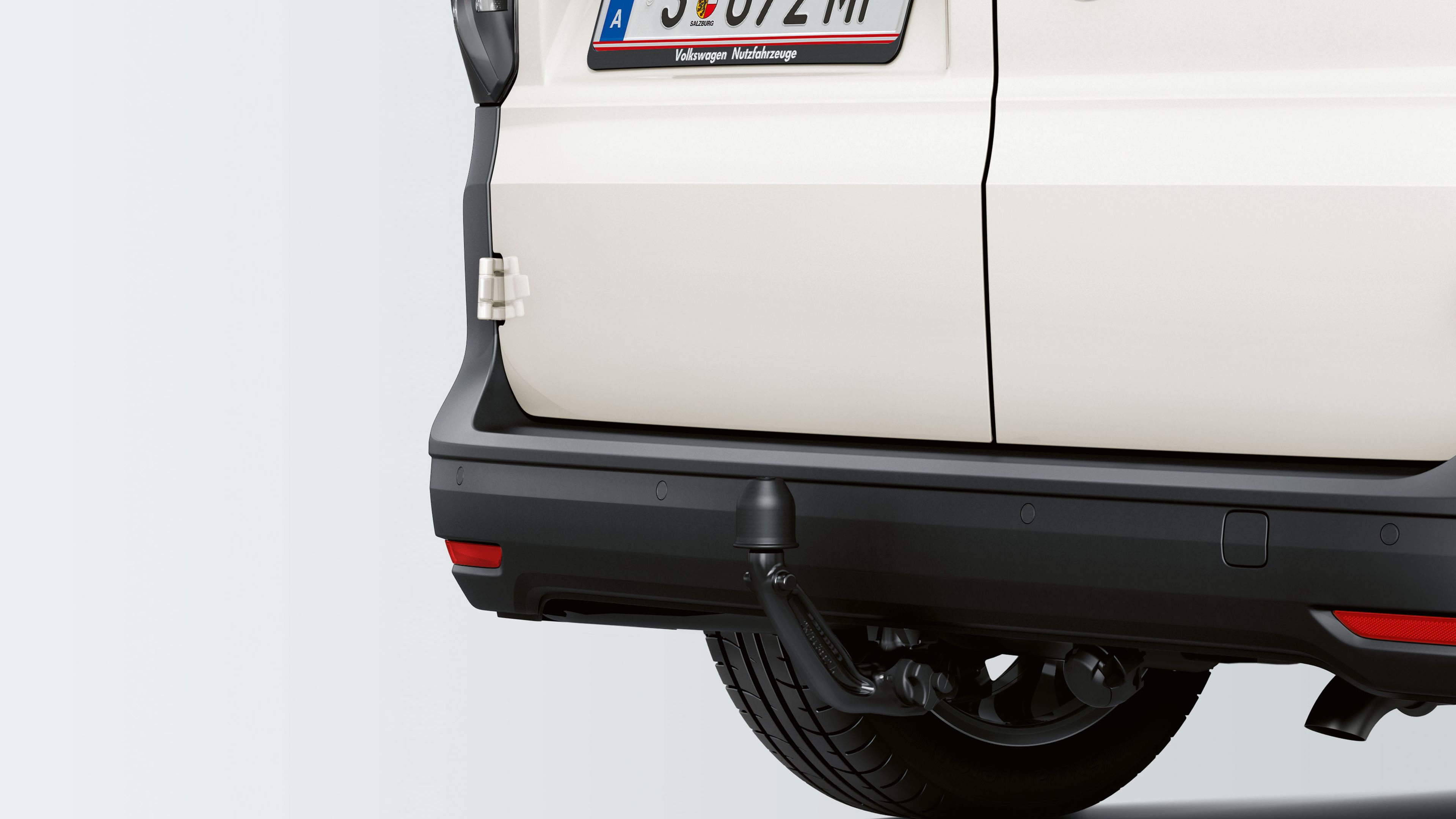 Zadná časť bieleho Volkswagen Caddy s rakúskou poznávacou značkou "SE 672 MI". Viditeľné sú zadné svetlá a náhradné koleso.