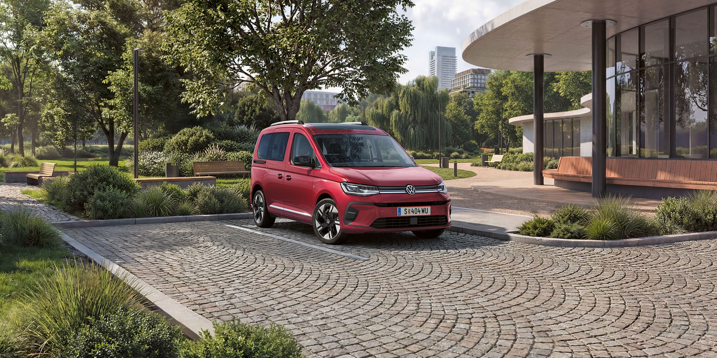 Nový červený Caddy Style stojí na ceste dláždenej ploche pred budovou. 