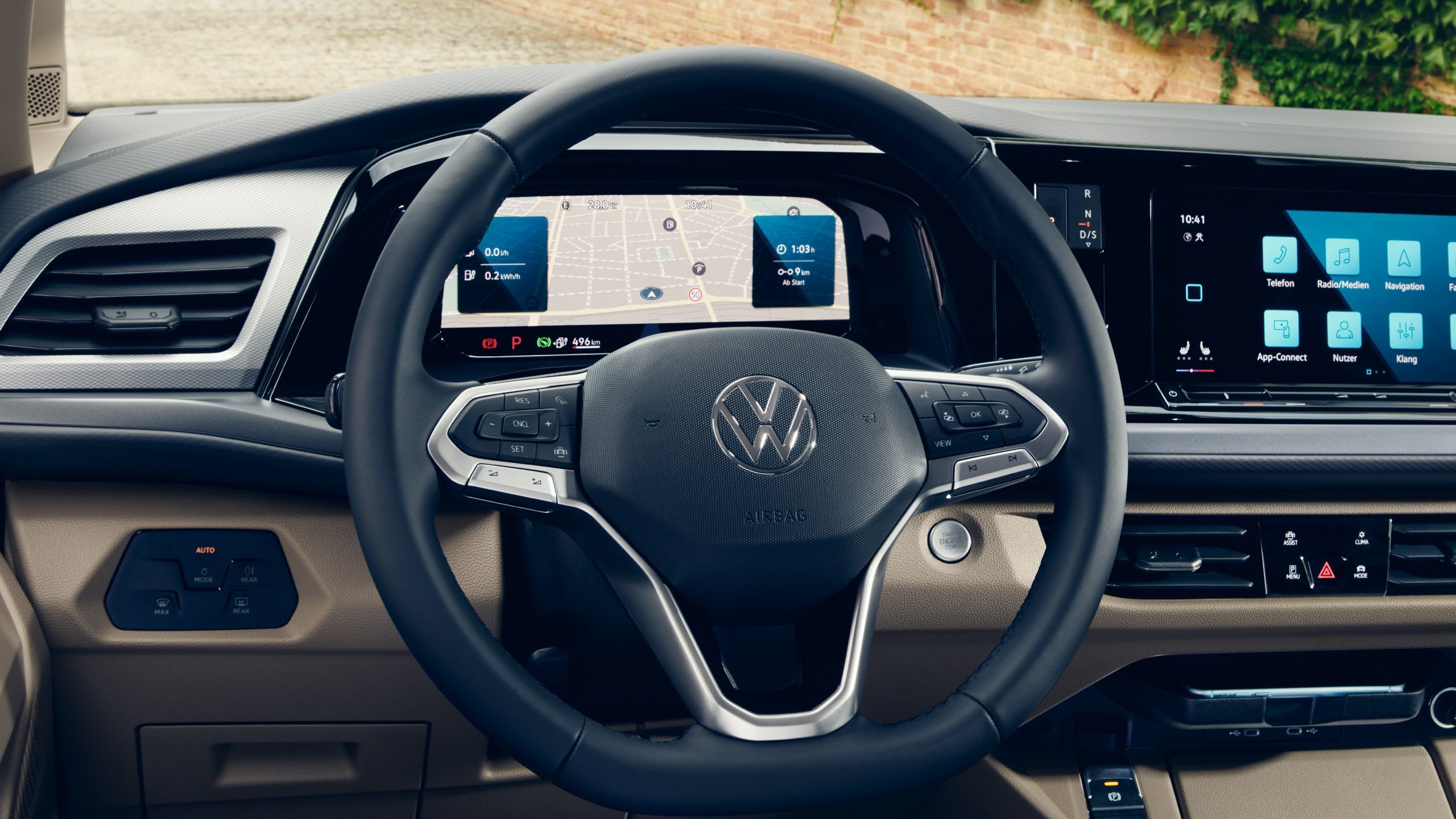 Interiér auta značky Volkswagen, detail na multifunkčný volant. Na digitálnom prístrojovom paneli sú zobrazené navigačné pokyny. Interiér má moderný dizajn s rôznymi ovládacími prvkami.
