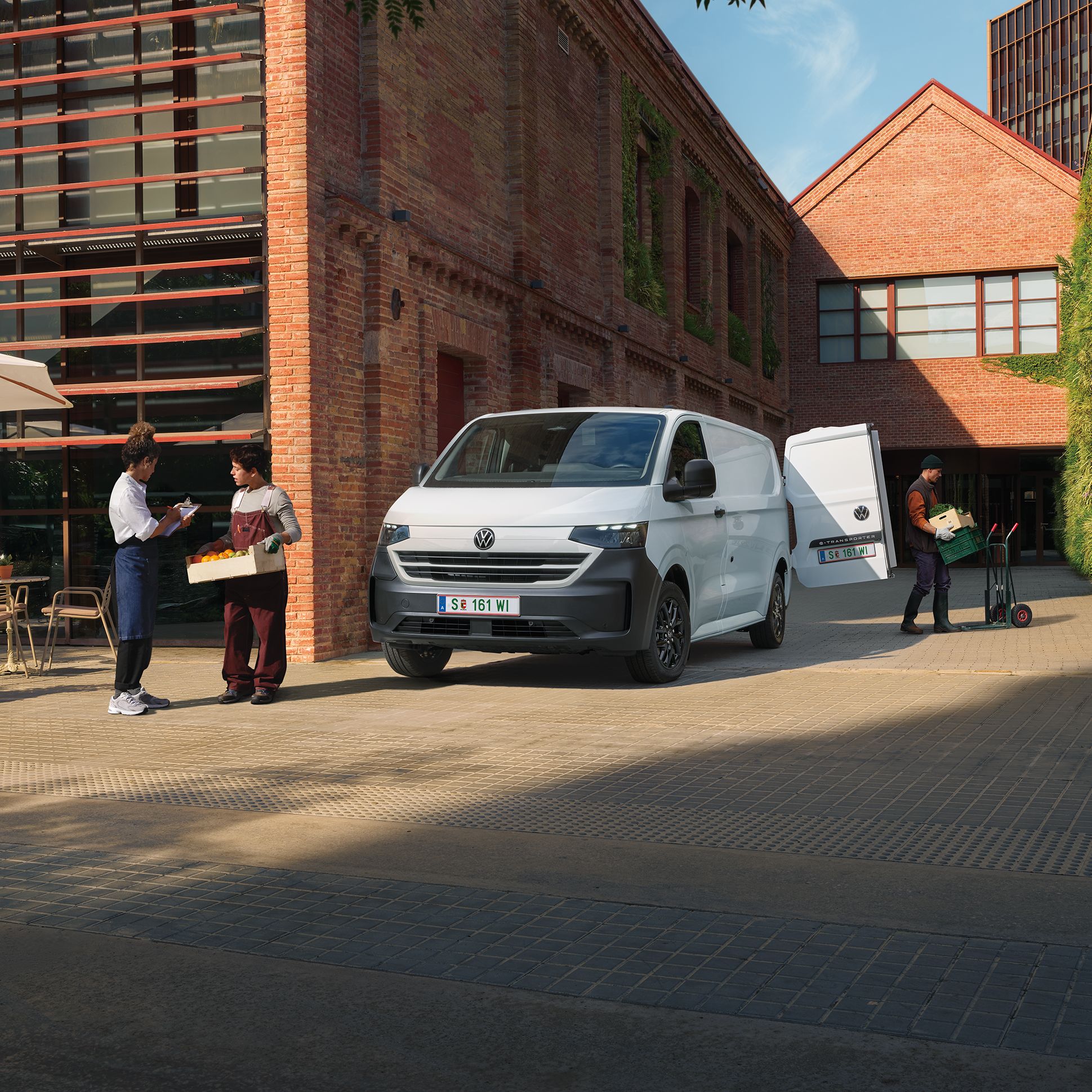 Pred tehlovou budovou stojí biela dodávka VW Transporter. Budova je staršia, prerobená a má industriálny charakter s modernými prvkami.