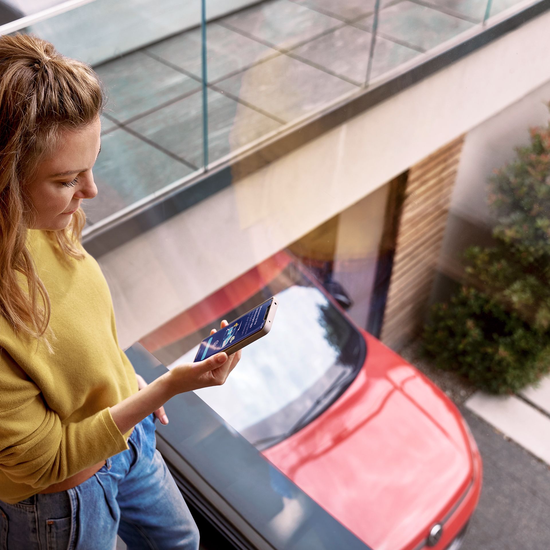 Žena sa prihlasuje do zákazníckeho portálu myVolkswagen na svojom smartfóne, v pozadí je auto značky VW.